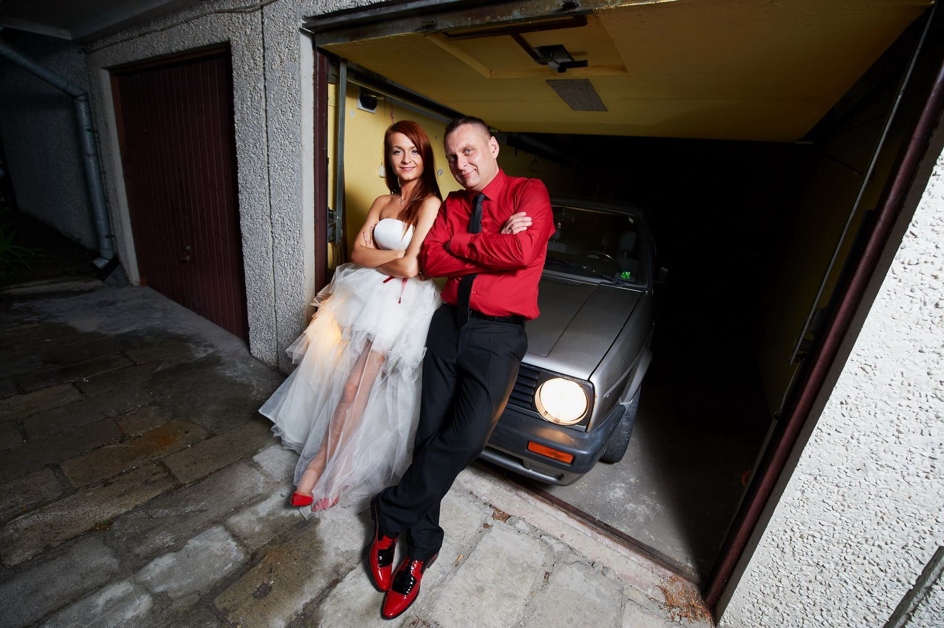 Explore bold wedding fashion with this image of a couple rocking red shoes and unconventional attire in a garage setting. Perfect for inspiration on making a statement on your big day.